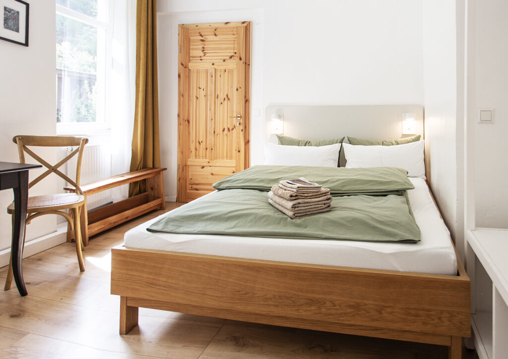Blick auf das Bett im Ferien Apartment in den Farben des Waldes. Grüne Bettwäsche und Holz.